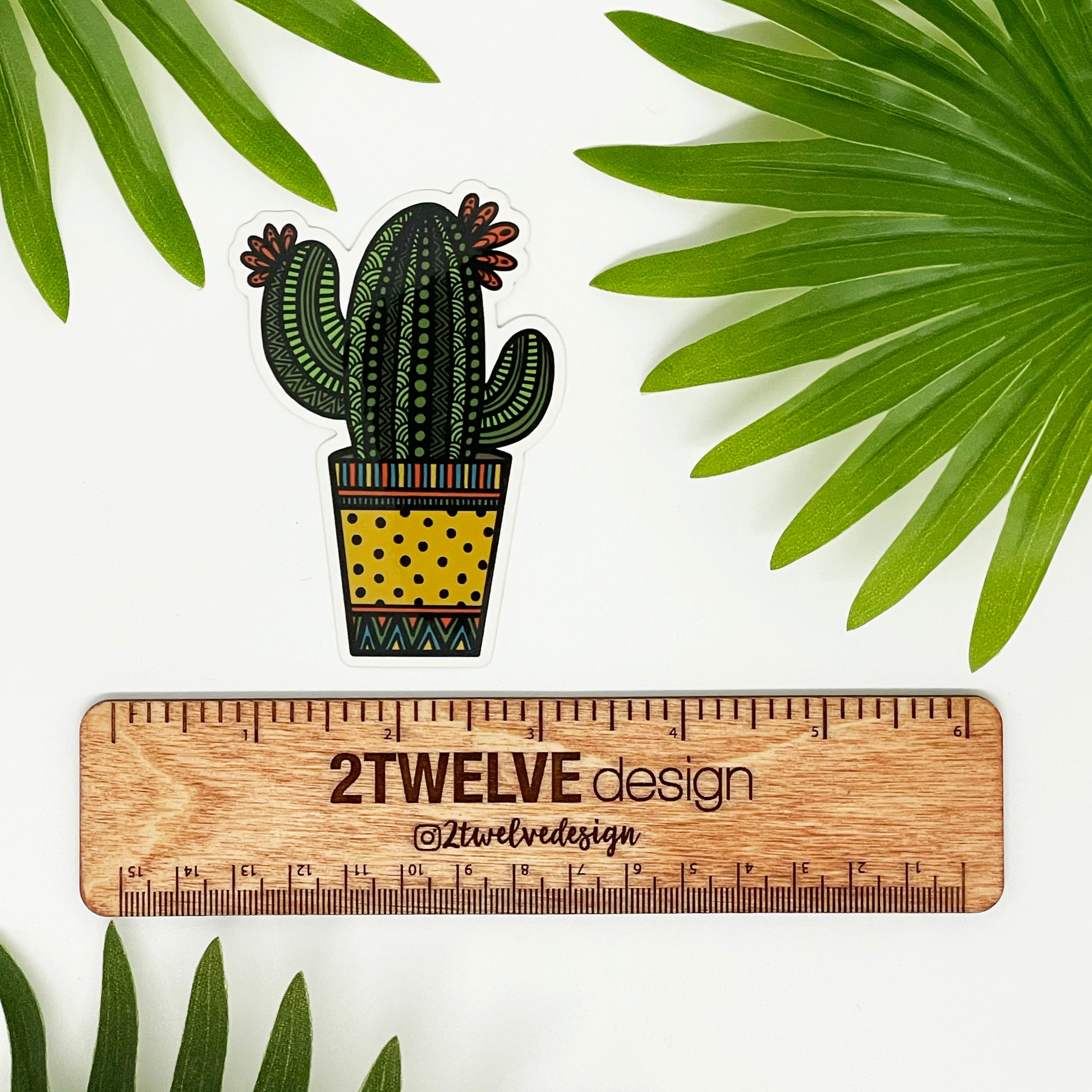 A cute and spunky cactus illustration made into a vinyl sticker. Laying on a white background with leaves surrounding and a ruler to determine actual size.