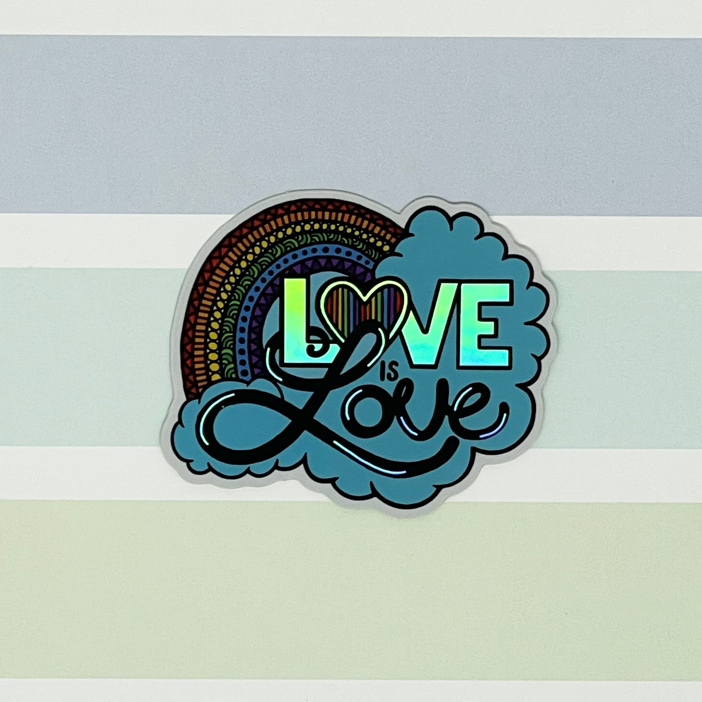 A cute Love is Love illustration with a rainbow and clouds turned into a die-cut sticker. Laying on a patterned background.