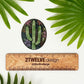 A floral and cactus oval sticker. Pastel colors and cute details. Laying above a "2Twelve Design" ruler on a white background surrounded by palm leaves. 