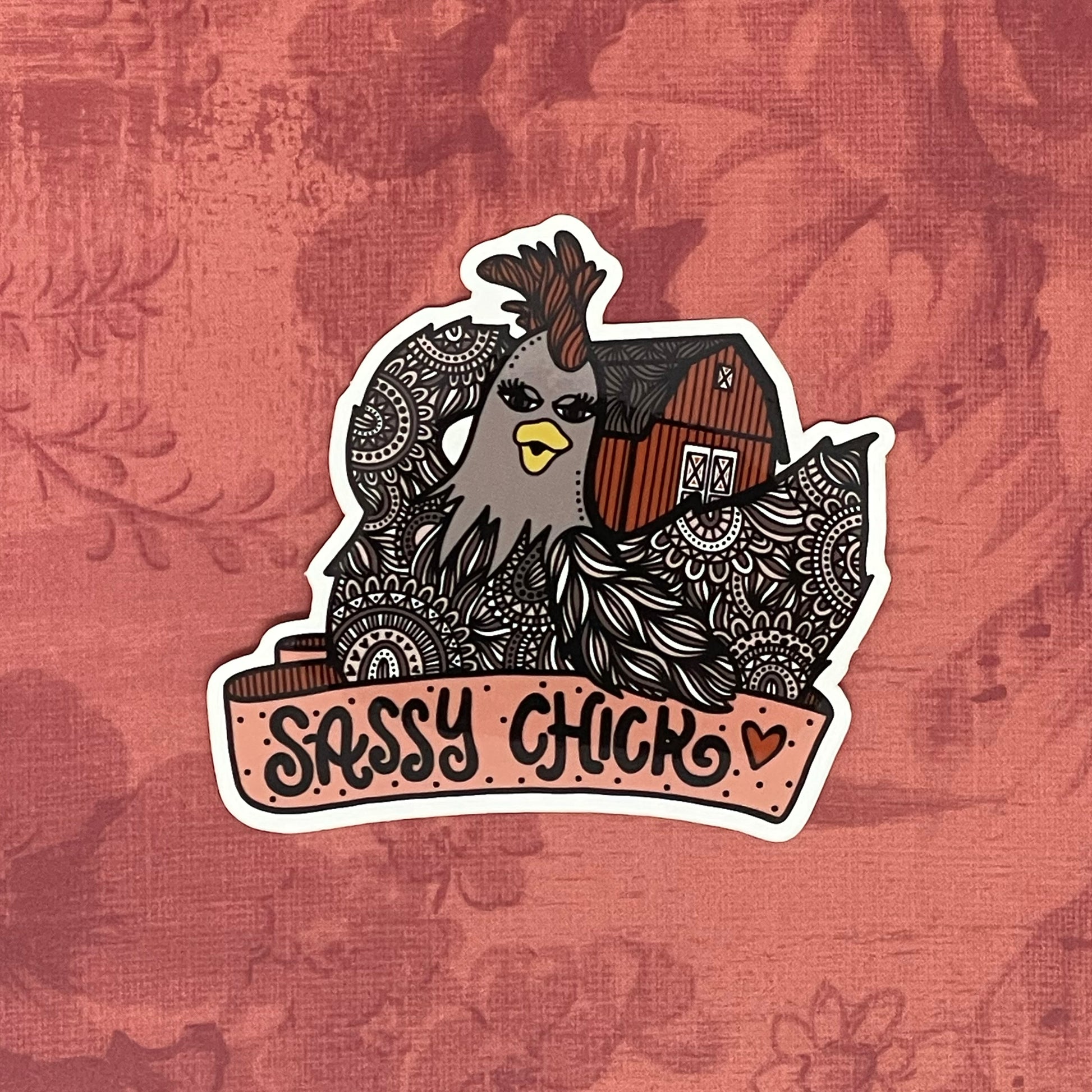 A cute chicken and barn illustration with a banner that reads "Sassy Chick", made into a vinyl sticker. Laying on a red texture background.