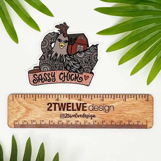 A hand drawn chicken and barn illustration with a "Sassy Chick" banner. Laying on a white background above a "2Twelve Design ruler" surrounded by palm leaves.