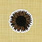 A very detailed sunflower illustration made into a die-cut matte sticker. Laying on a patterned yellow background.