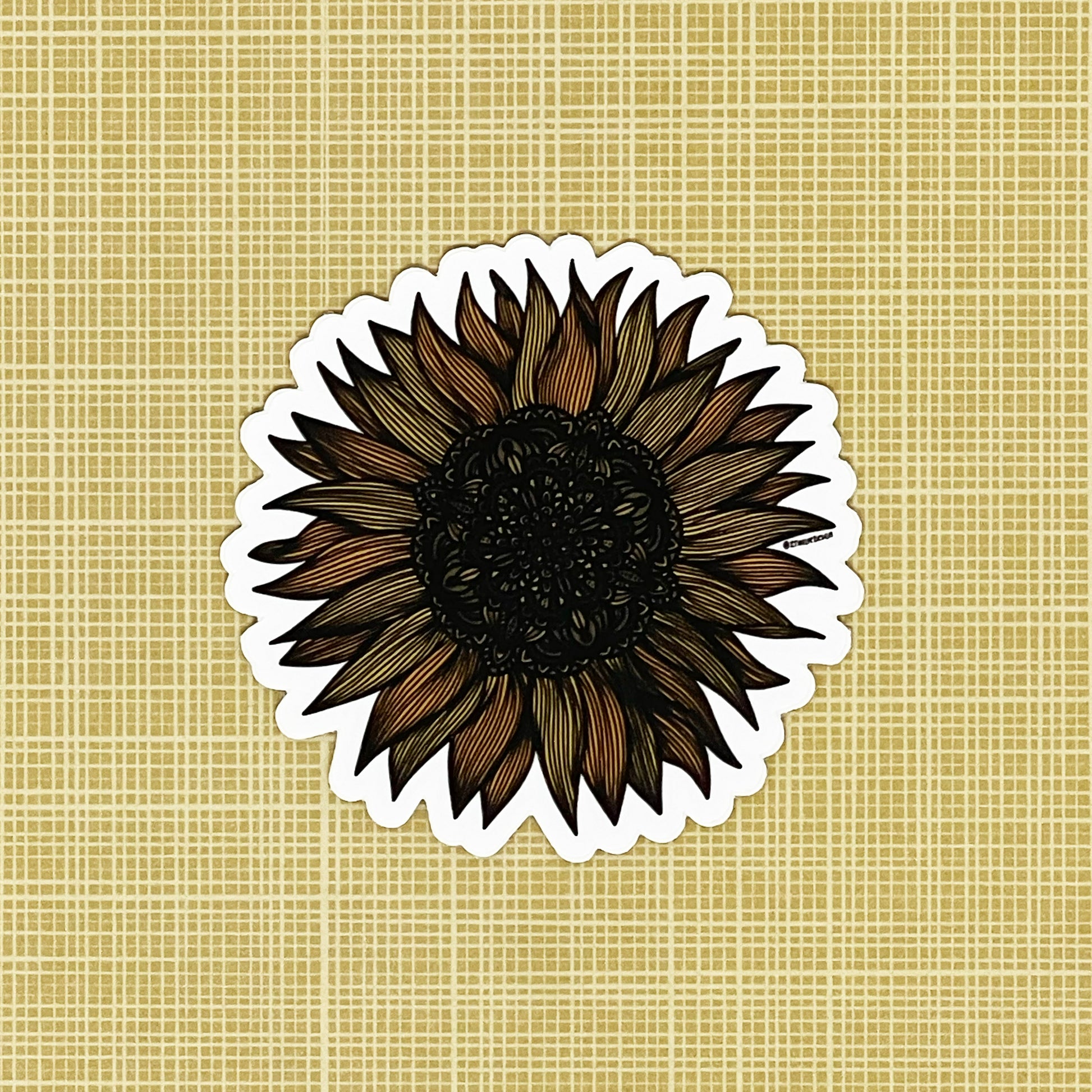 A very detailed sunflower illustration made into a die-cut matte sticker. Laying on a patterned yellow background.