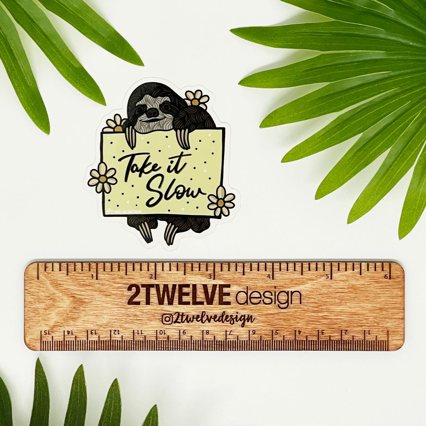 A sticker of a hand drawn sloth holding a sign that says "Take It Slow" 