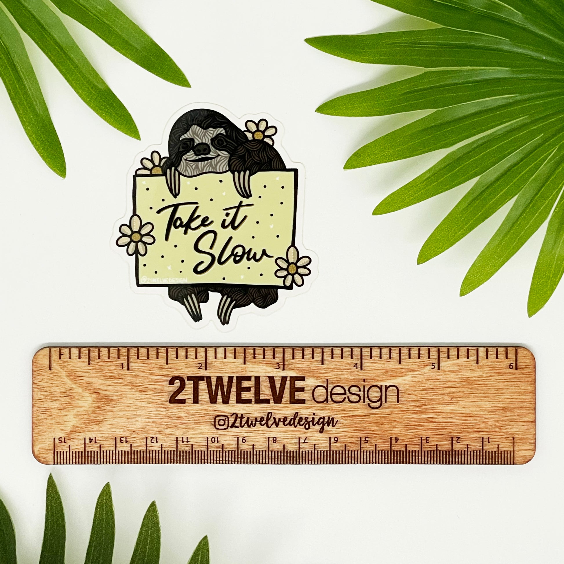 A sticker of a hand drawn sloth holding a sign that says "Take It Slow" 