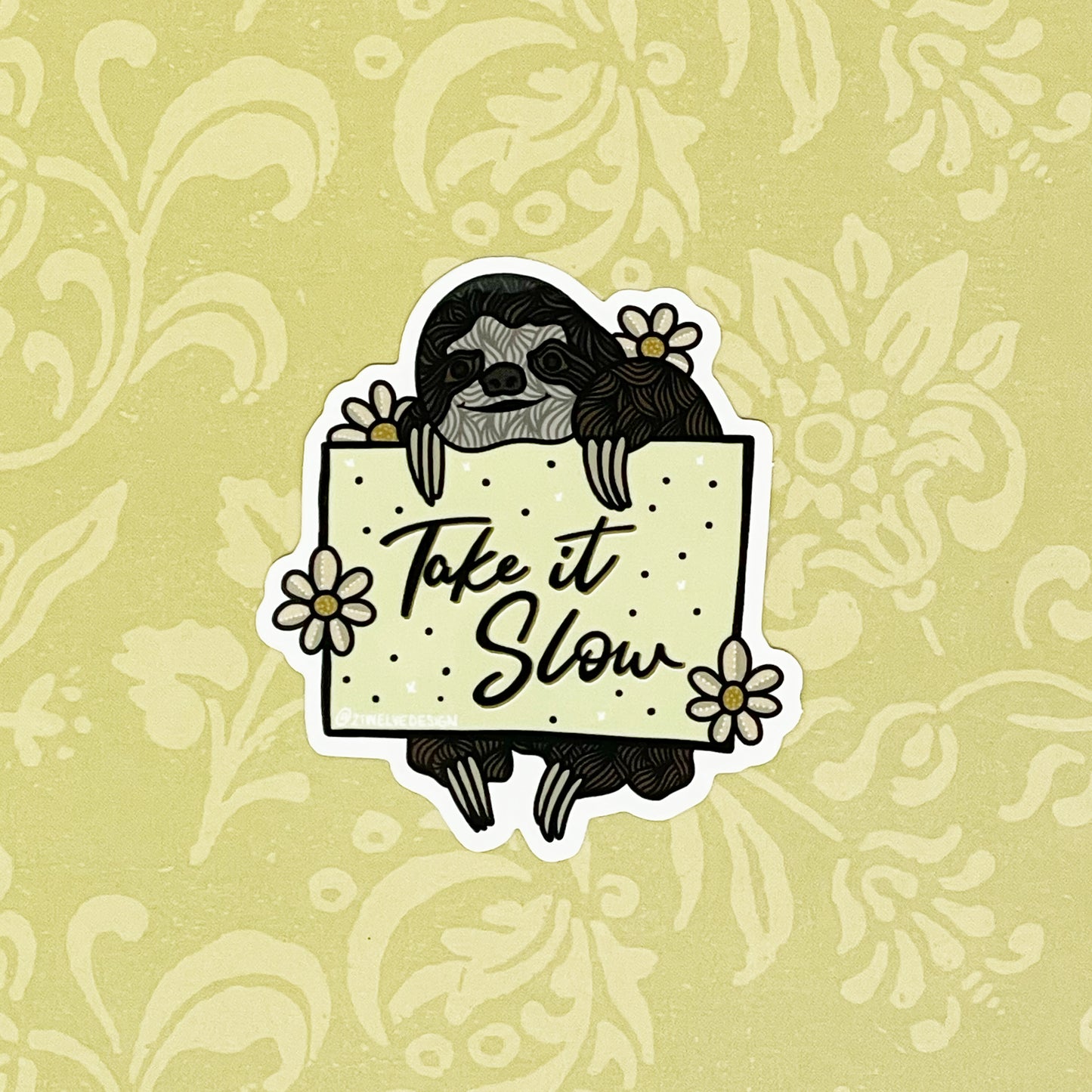 A sticker of a sloth holding a sign with "Take It Slow" written on it. Laying on a light yellow background.