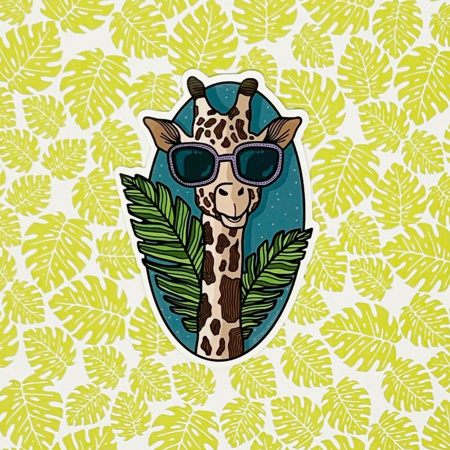 A cool, tropical giraffe illustration made into a durable vinyl sticker. Laying on a background of neon green leaves.