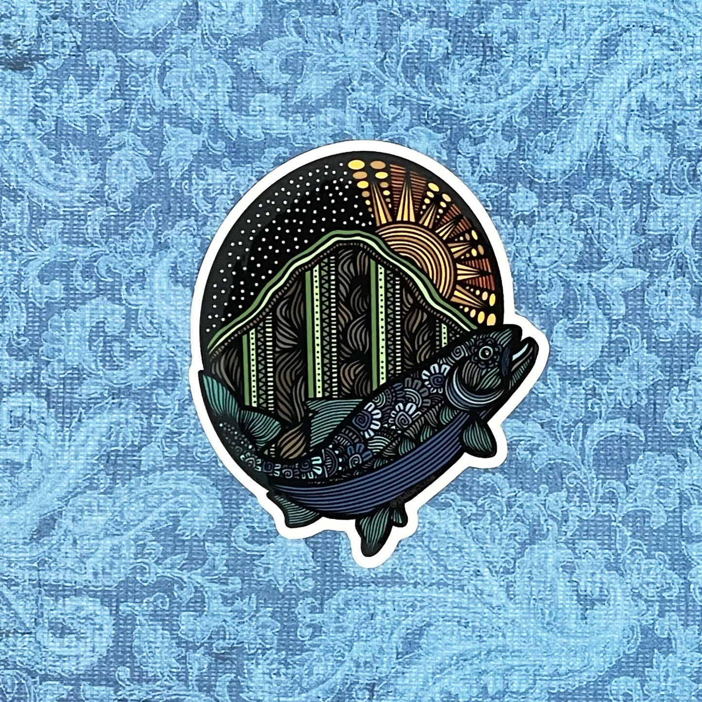 An illustration of a salmon and mountain made into a colorful sticker. Laying on a blue pattern background.