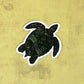 Detailed turtle illustration made into a sticker laying on a yellow textured surface.