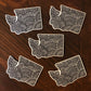 A group of five WA state diecut stickers laying on a wooden surface.