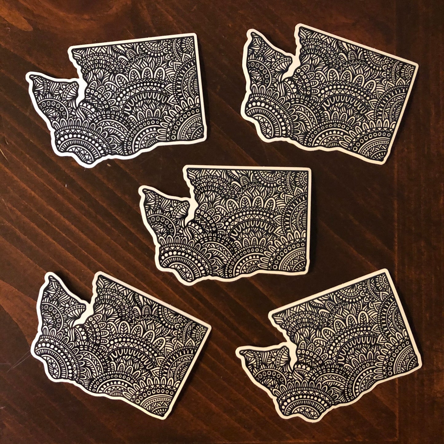 A group of five WA state diecut stickers laying on a wooden surface.