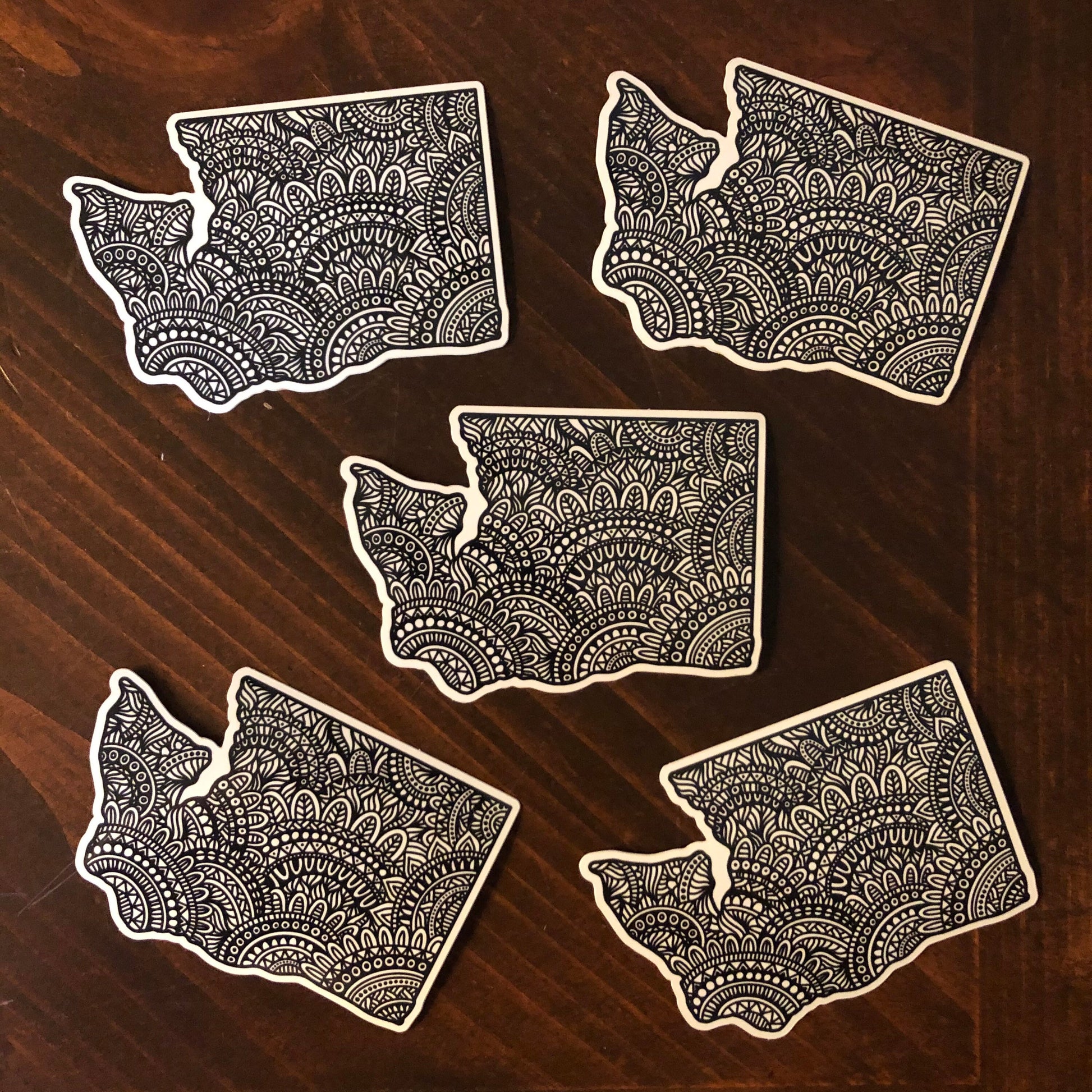 A group of five WA state diecut stickers laying on a wooden surface.