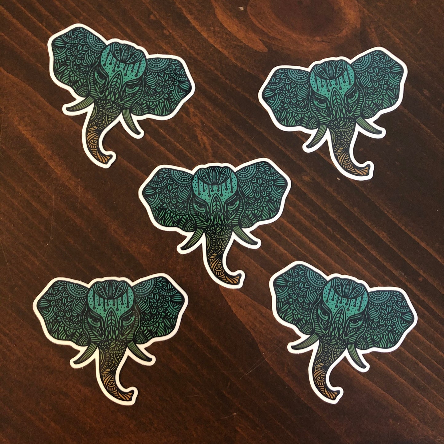 A group of five, detailed illustrated elephant stickers laying on a wooden surface